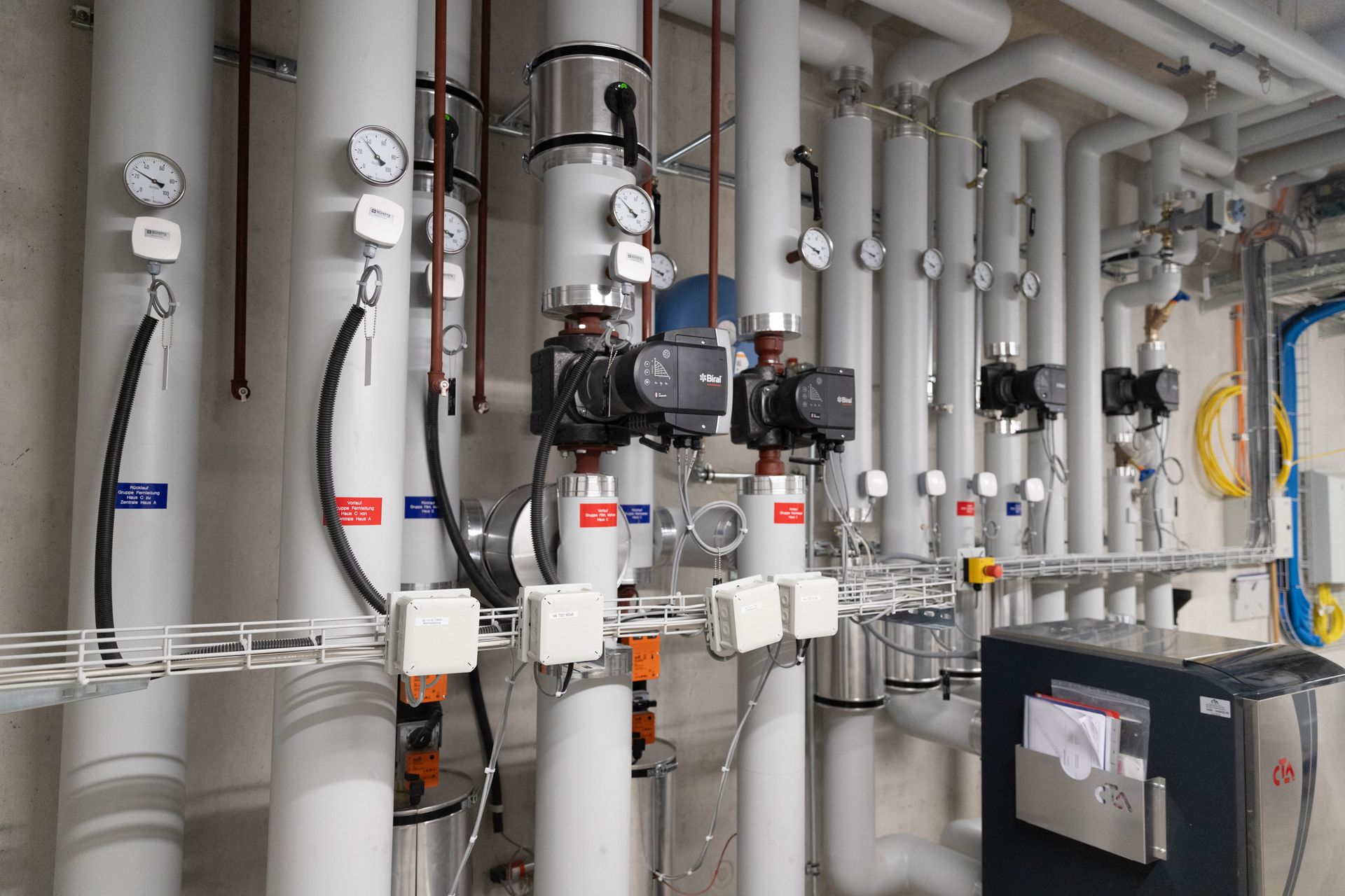 Rohre und Maschinen in einer industriellen Umgebung. Die Rohre sind weiß mit schwarzen Pumpen und verschiedenen Messgeräten.