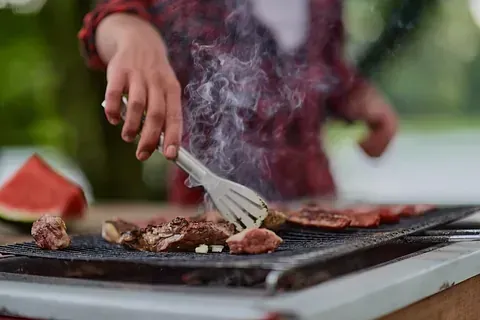 Una persona está cocinando carne en una parrilla con una espátula.