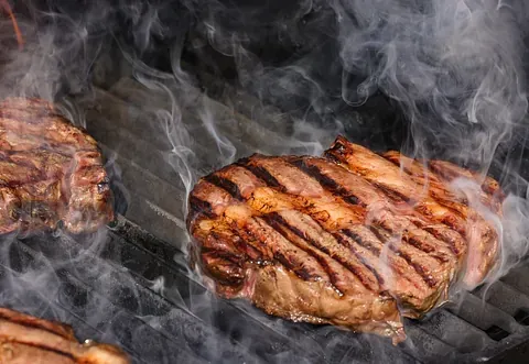 Tres filetes se cocinan en una parrilla y sale humo de ellos.