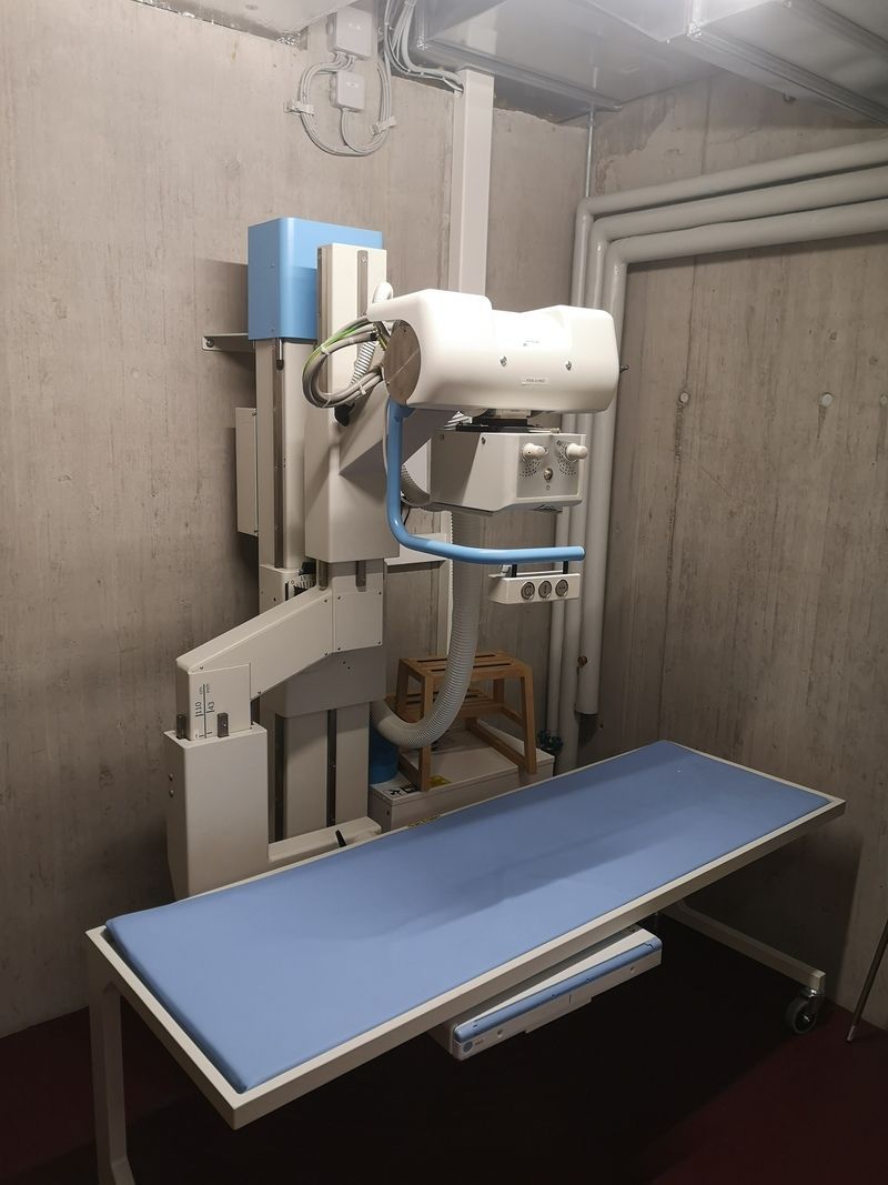 Une machine à rayons X est installée dans une pièce avec une table bleue.