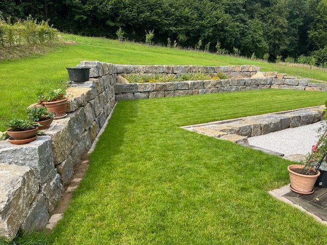 Ein üppiger grüner Rasen mit einer Steinmauer und Topfpflanzen.