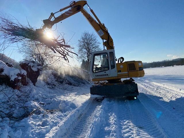 Ein gelber Bagger fährt eine verschneite Straße entlang.