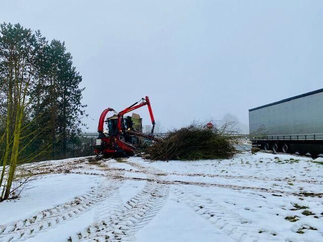 Ein schneebedecktes Feld mit einem LKW im Hintergrund und einem Traktor im Vordergrund.