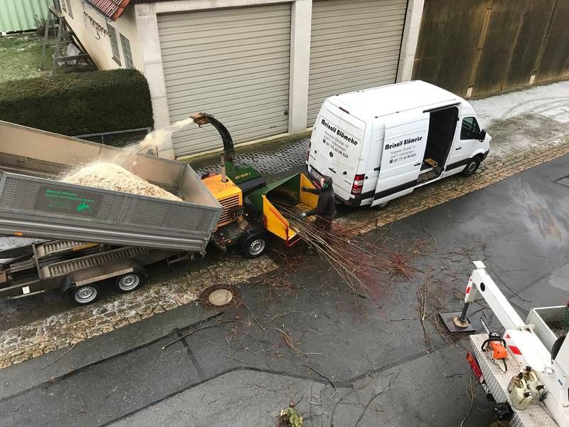 Ein weißer Lieferwagen steht am Straßenrand neben einem Baumhäcksler.