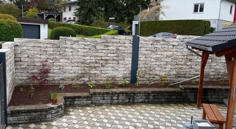 Eine Backsteinmauer umgibt eine Terrasse mit einer Bank und einem Pavillon.