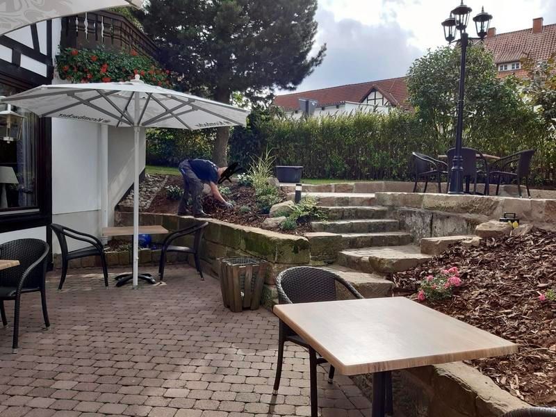 Ein Mann arbeitet auf einer Terrasse mit Tischen und Stühlen unter einem Sonnenschirm