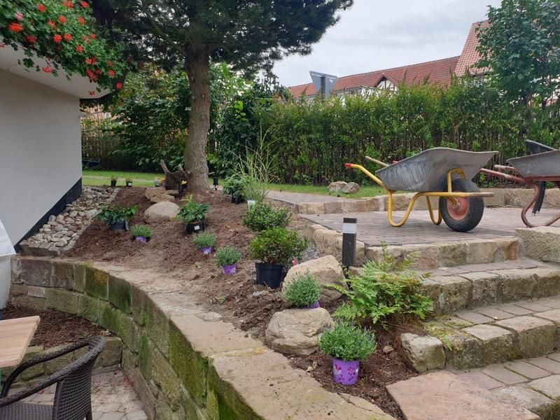 Eine Schubkarre steht in einem Garten neben einer Steinmauer.