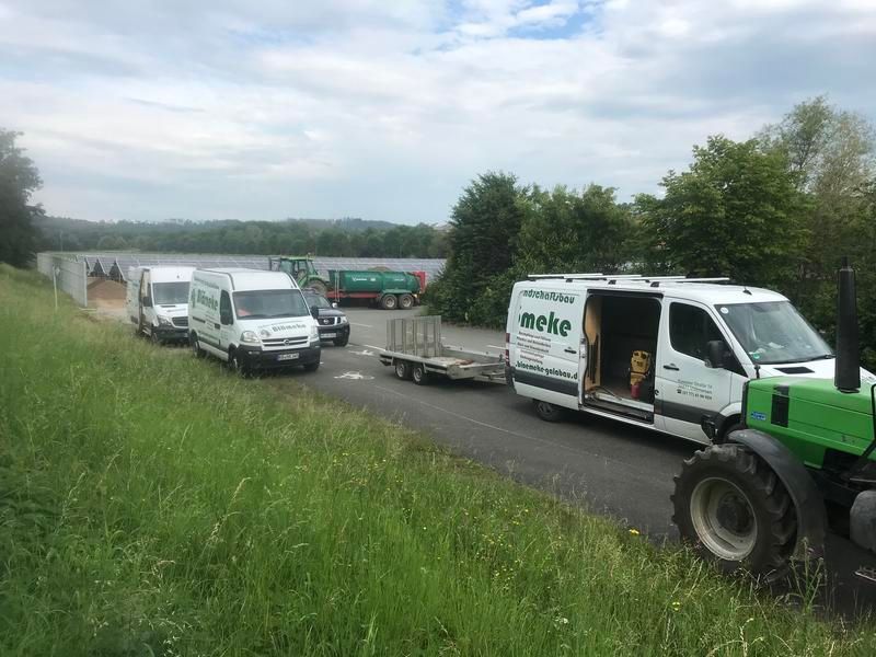 Eine Reihe Lieferwagen parkt am Straßenrand neben einem Traktor.