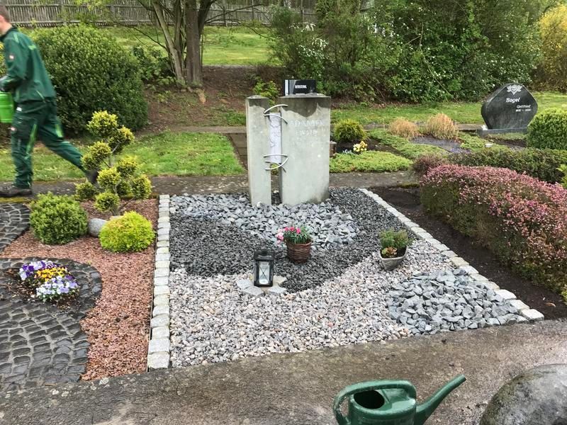 Ein Mann bewässert einen Friedhof mit einer grünen Gießkanne.