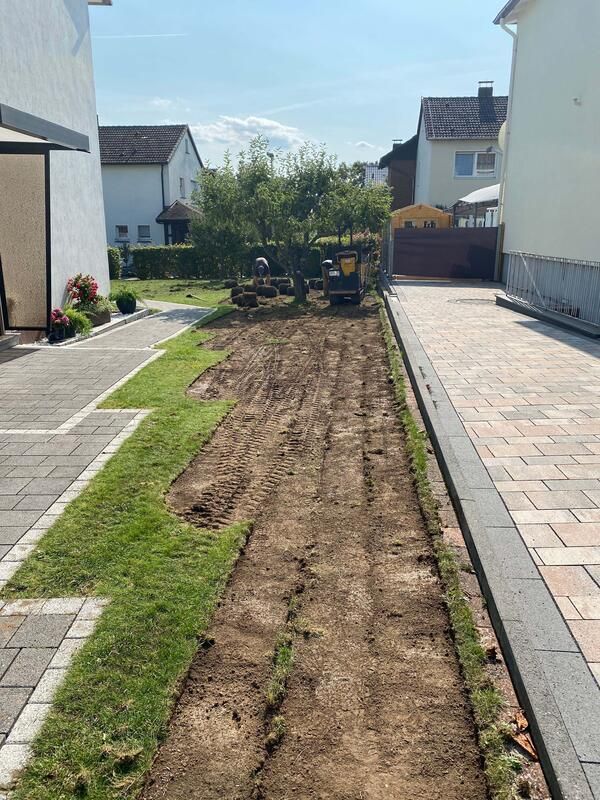 Ein Traktor bewegt Erde in einer Einfahrt neben einem Haus.