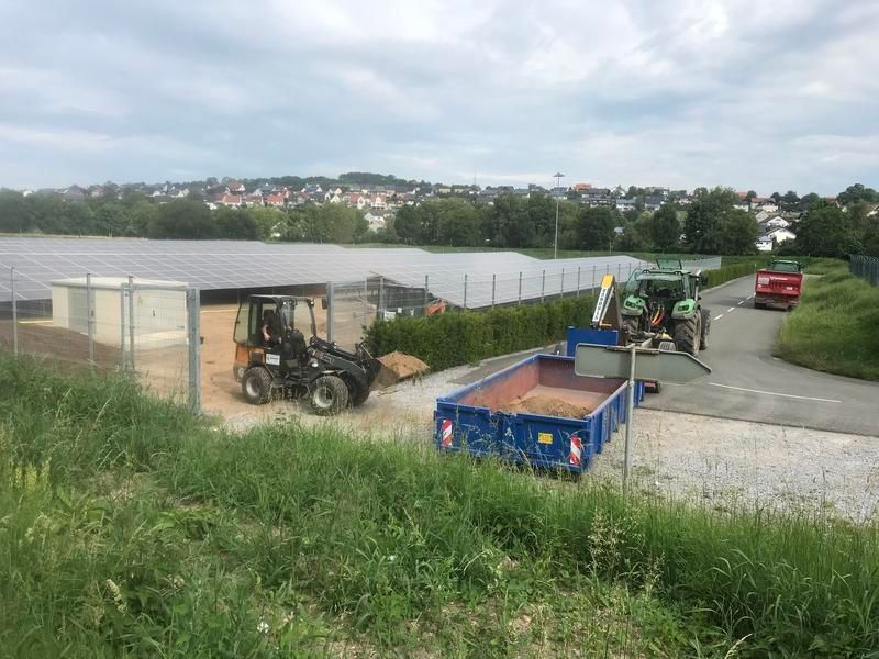 Ein Traktor fährt auf einer unbefestigten Straße neben einem blauen Müllcontainer her.