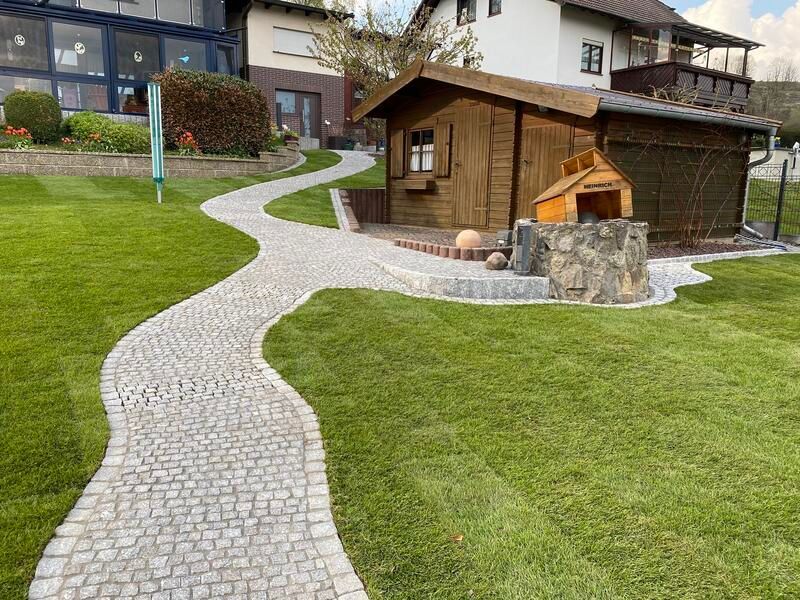 Ein Steinweg führt zu einem Holzschuppen in einem üppig grünen Hof.