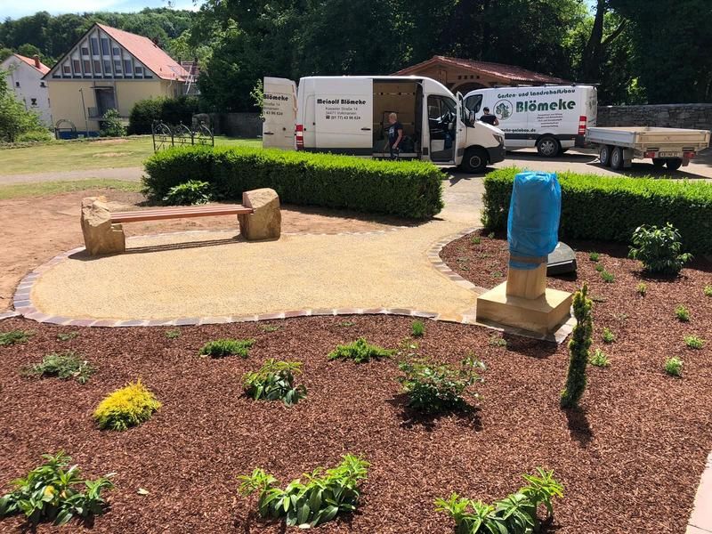 Ein weißer Lieferwagen steht in einem Garten neben einer Bank.