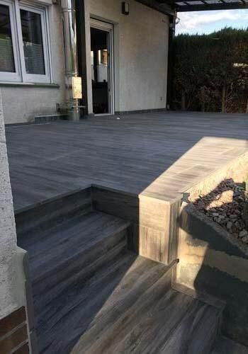 Vor einem Haus eine Holzterrasse mit einer Treppe, die dorthin führt.