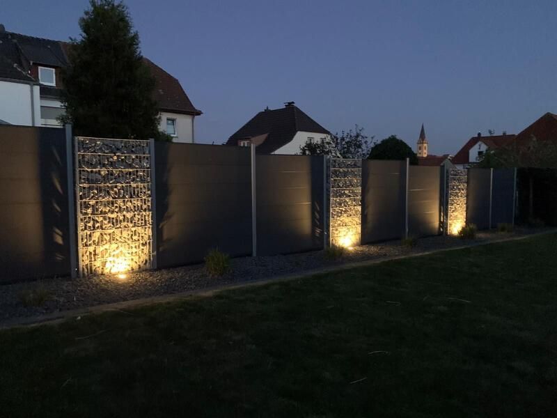 Ein Zaun ist nachts beleuchtet, im Hintergrund sind Häuser zu sehen