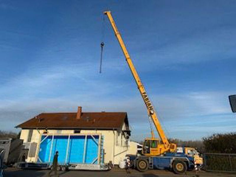 Ein großer gelber Kran hebt einen Pool vor einem Haus an.