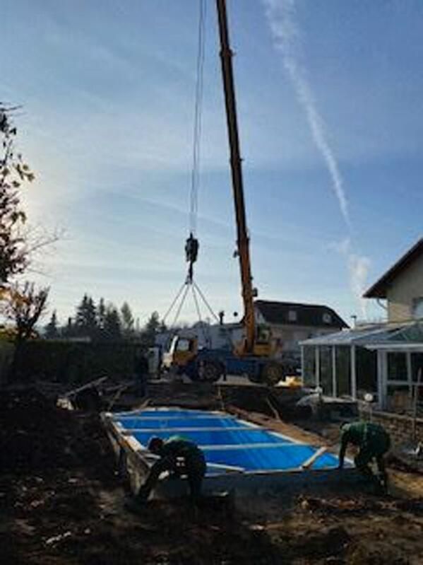 Ein Kran hebt einen Swimmingpool in einem Hinterhof an.