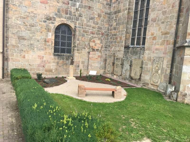 Vor einem Backsteingebäude steht mitten im Gras eine Bank.