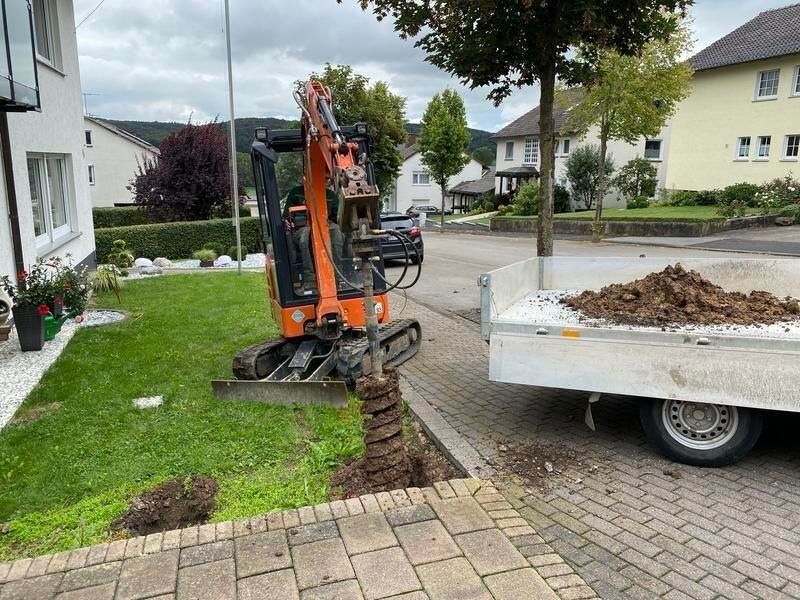 Ein kleiner Bagger gräbt vor einem Haus ein Loch in den Boden.