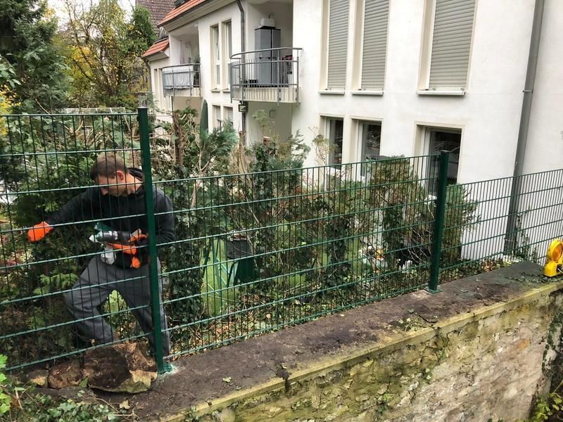 Ein Mann arbeitet an einem Zaun vor einem Haus