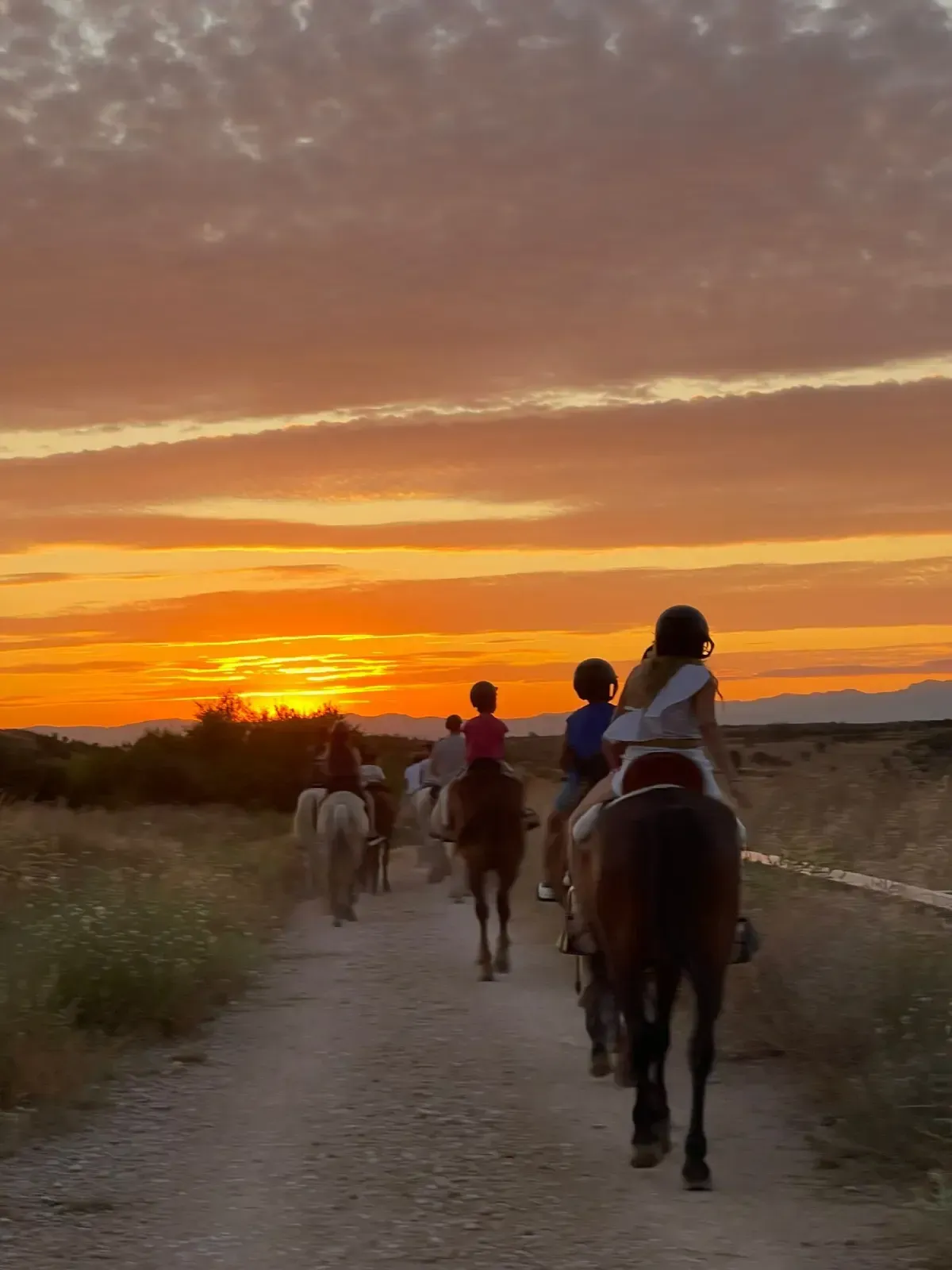 Grupo de personas cabalgando por un camino de tierra durante una vibrante puesta de sol.