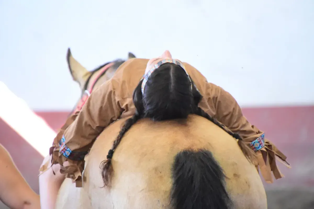 Una persona disfrazada yace boca abajo sobre el lomo de un caballo, cerca de la cabeza y la cola del caballo.