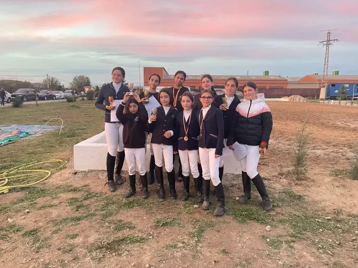 Grupo de jóvenes jinetes vestidos de montar posan al aire libre con trofeos.