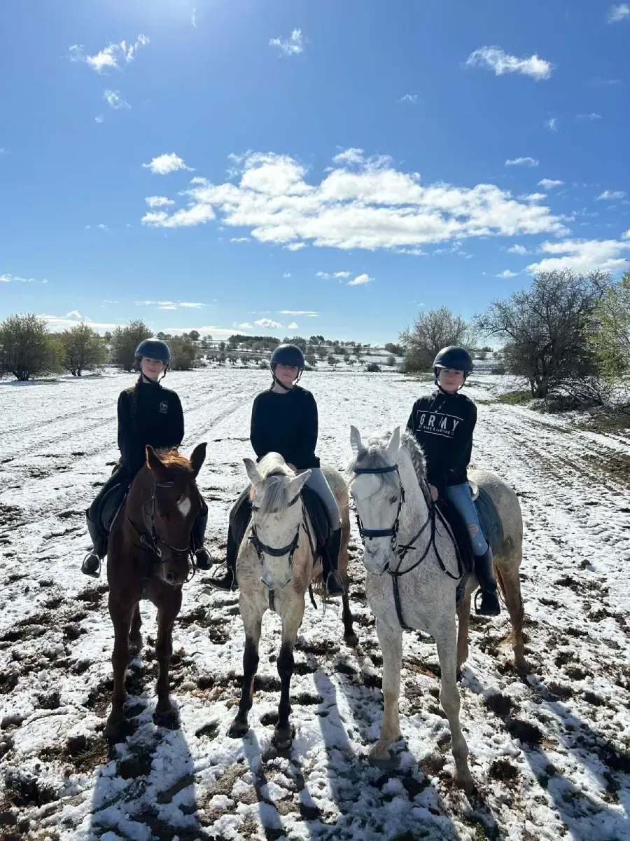 Tres personas a caballo en un campo nevado bajo un cielo azul.