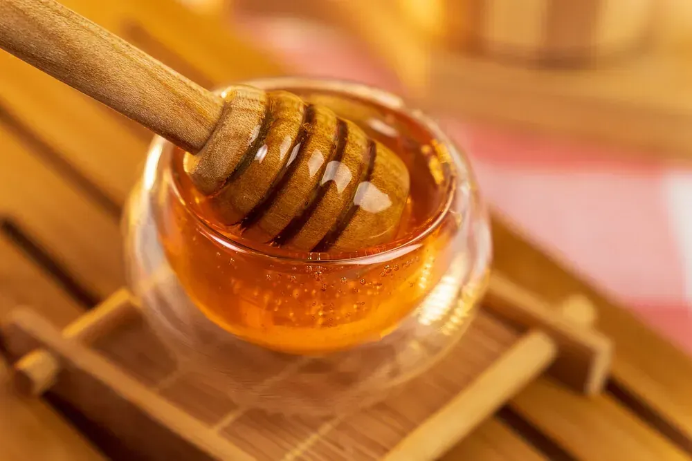 Un cucharón de miel sobresale de un vaso de miel.
