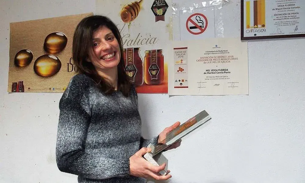 Una mujer sostiene un libro frente a una pared con carteles.