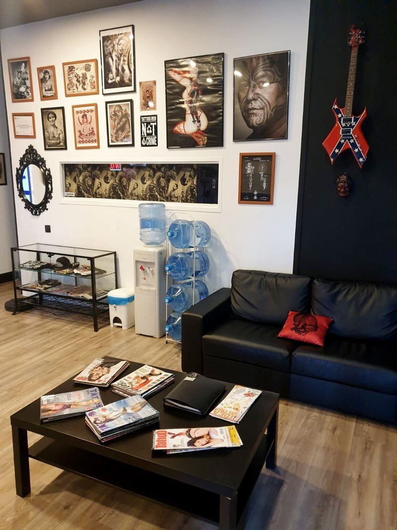 Una sala de espera con un sofá negro, una mesa de centro con revistas, un dispensador de agua, cuadros enmarcados en la pared y una vitrina con guitarras.