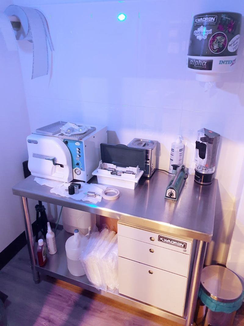 Una mesa de preparación de acero inoxidable en una clínica, equipada con un autoclave, suministros y cajones, bajo una iluminación brillante de tonos fríos.