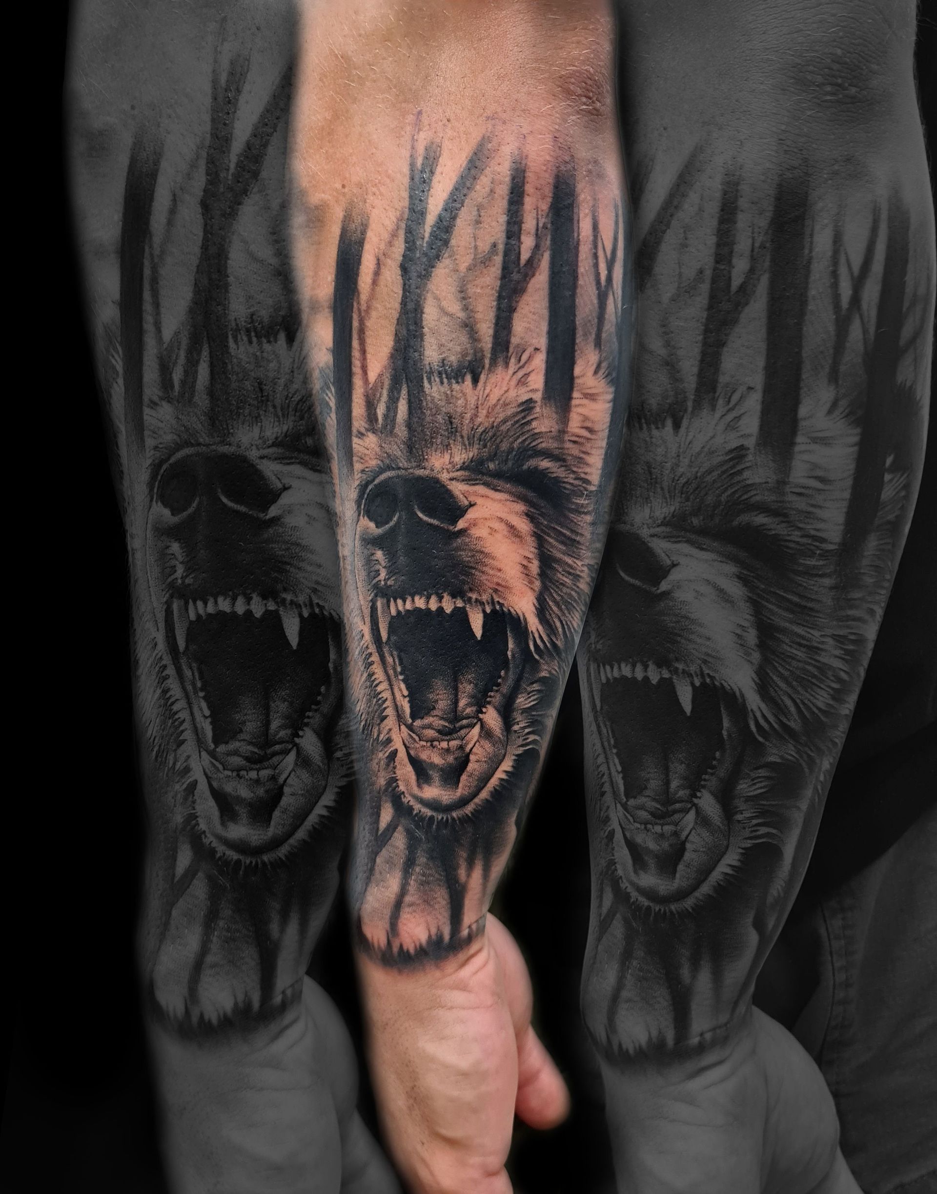 Primer plano de un tatuaje en el antebrazo que muestra un oso agresivo rodeado de siluetas de árboles oscuros y verticales del bosque.