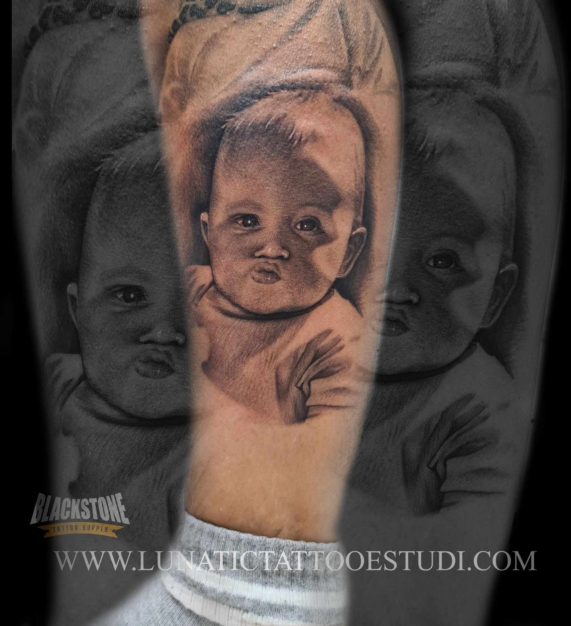 Tatuaje en blanco y negro del rostro de un bebé, realizado con sombreado fino en un brazo, con marca de agua y URL debajo.