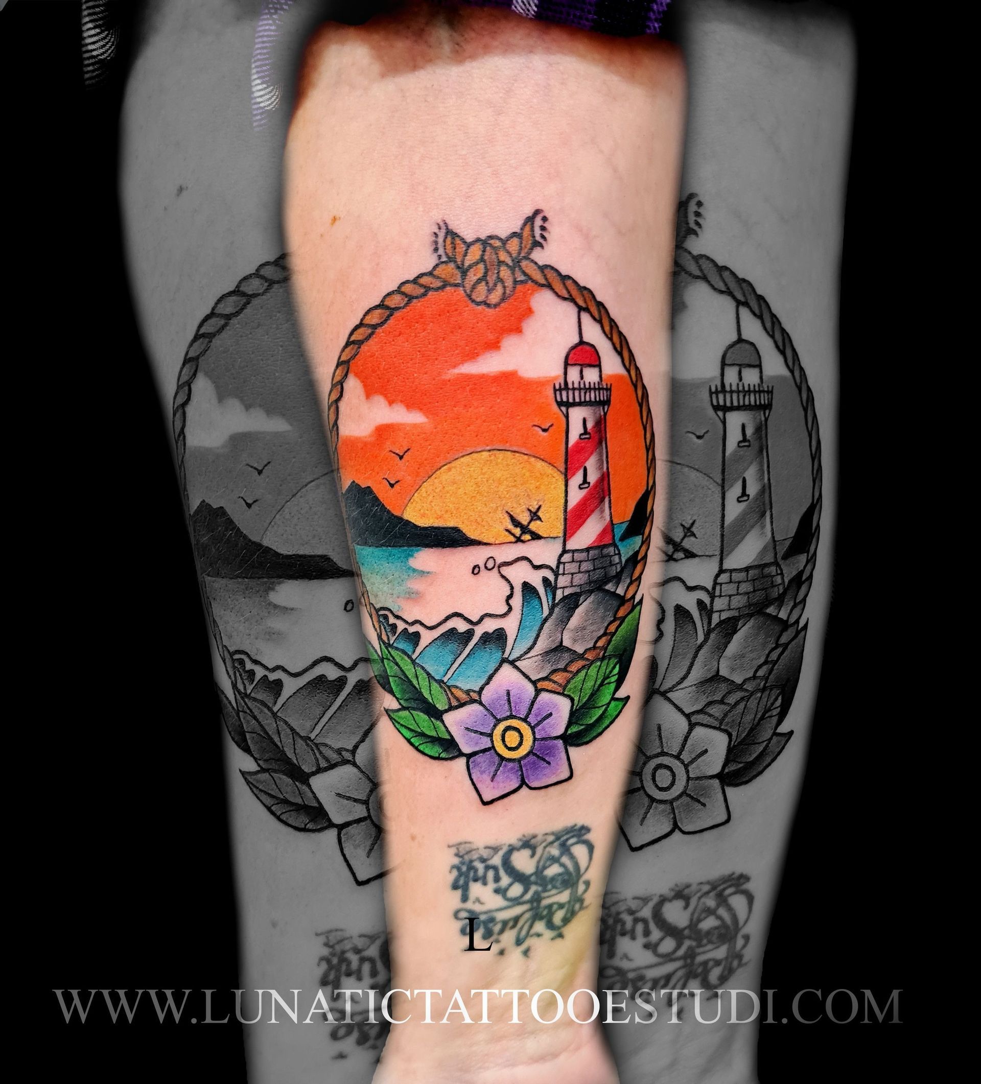 Un tatuaje a color en un brazo que muestra un faro, una puesta de sol y olas del océano, enmarcado por un borde de cuerda con una flor morada.