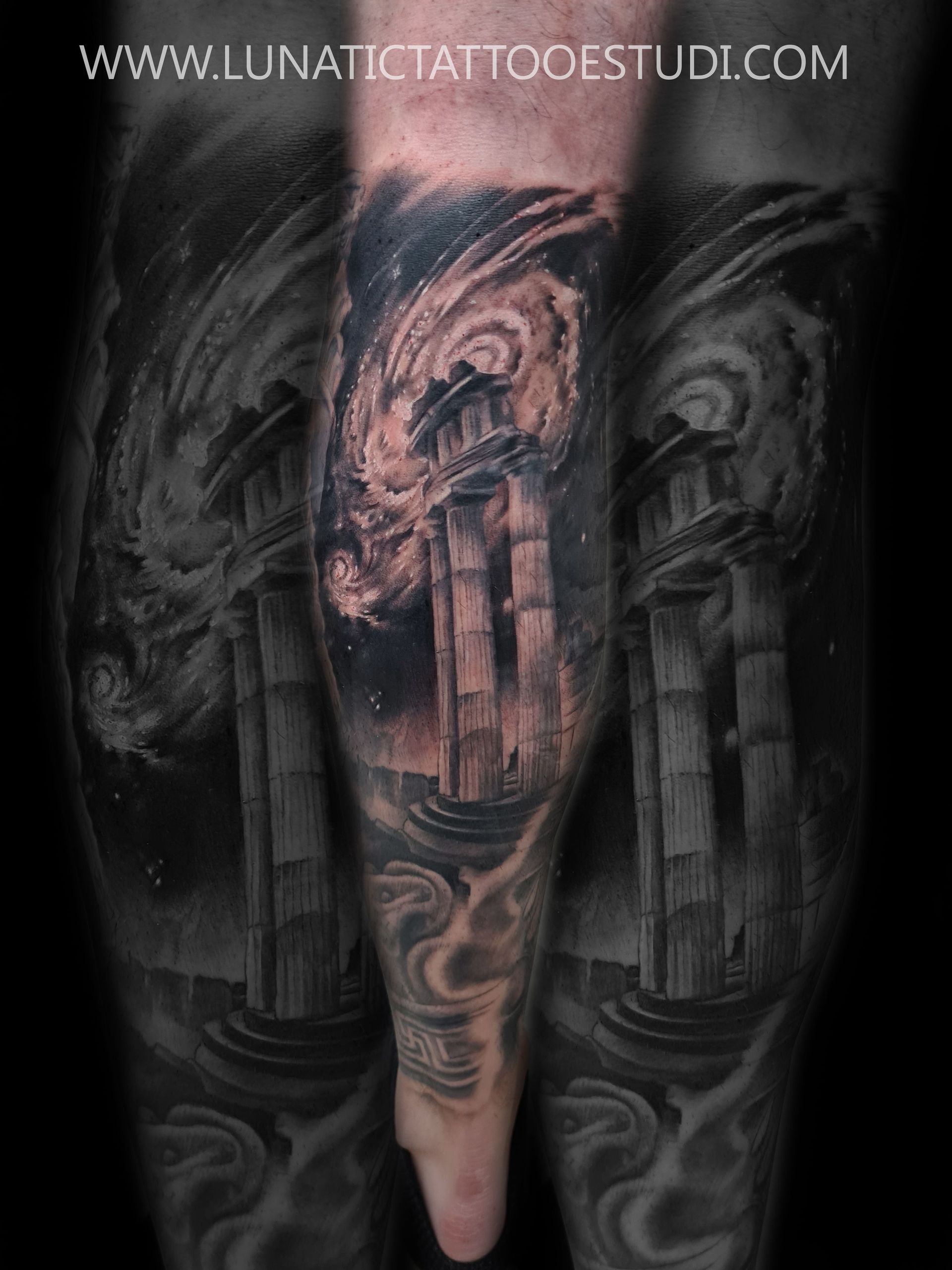 Tatuaje en blanco y negro de columnas griegas bajo una nebulosa cósmica en espiral en el brazo de una persona.