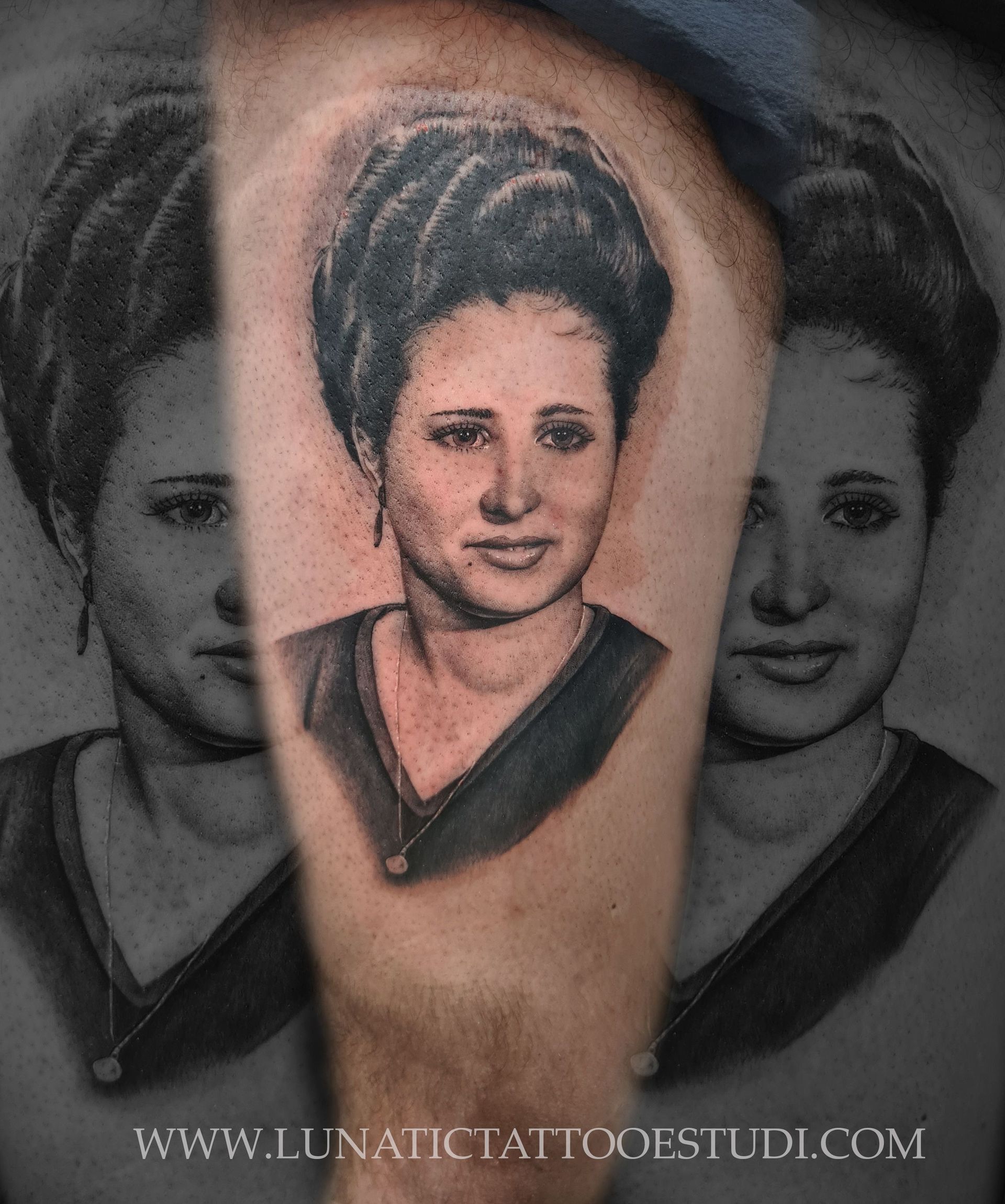Un tatuaje detallado en blanco y negro que representa el retrato de una persona con cabello oscuro, sobre un fondo borroso.