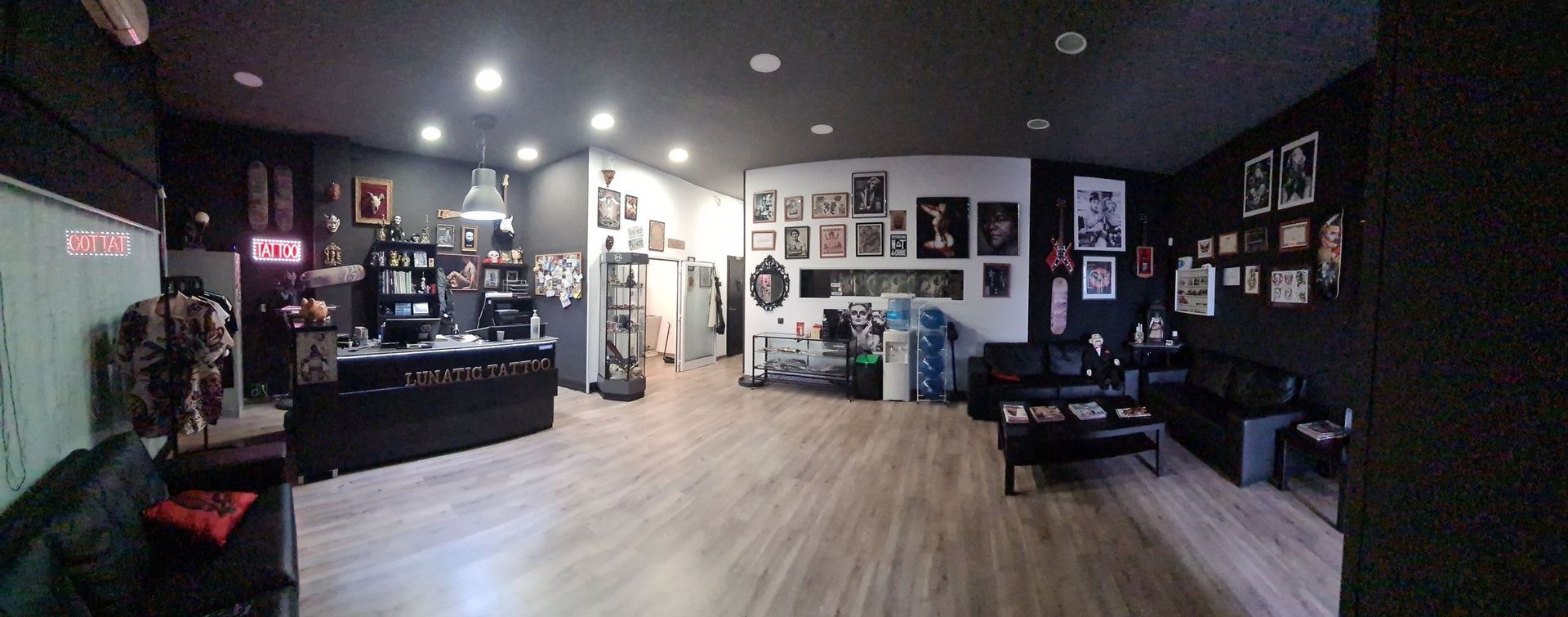 Un estudio de tatuajes amplio y moderno con mostrador de recepción, sofás de cuero negro y numerosas obras de arte enmarcadas en las paredes.