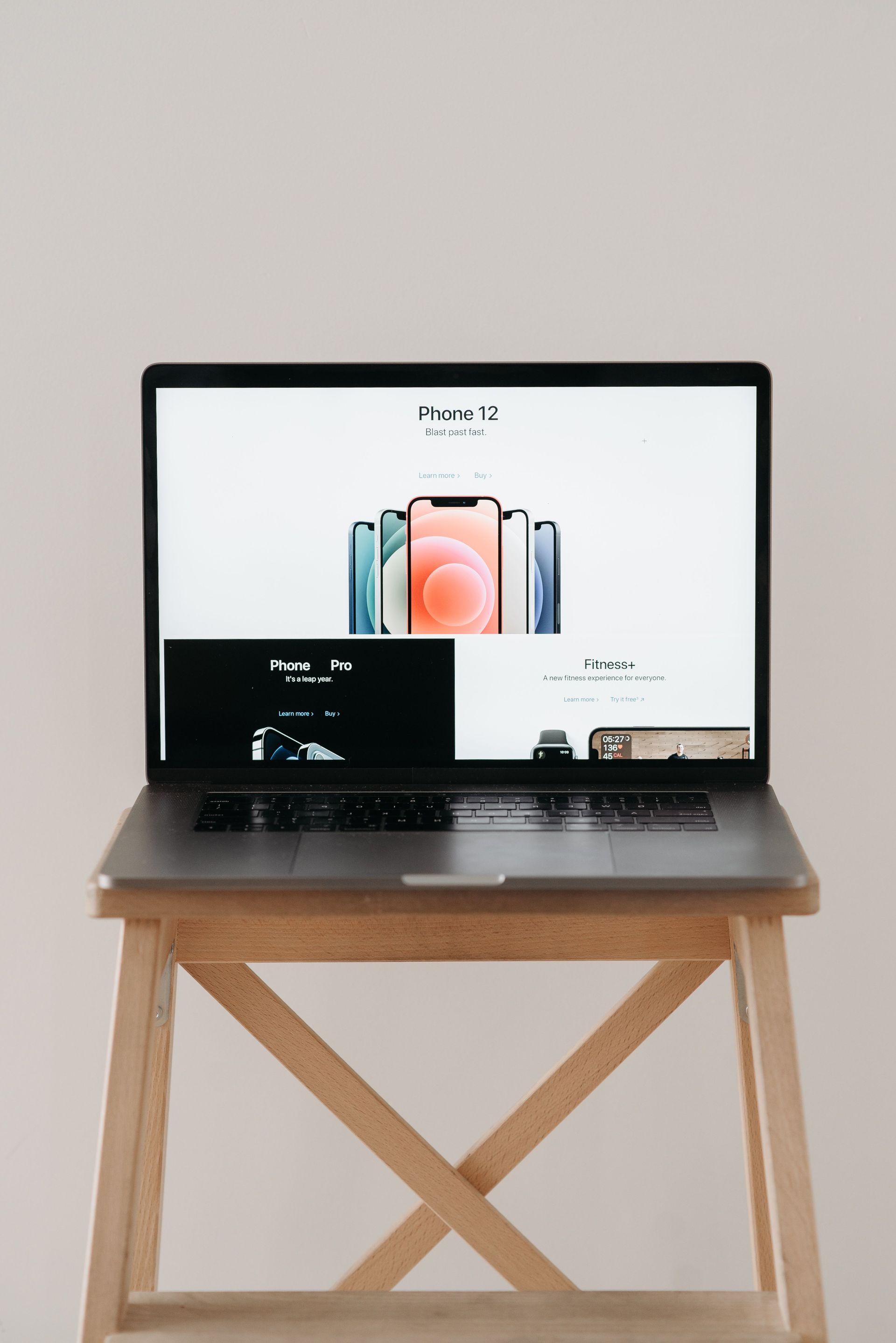 Un portátil sobre una mesa de madera muestra la página de un producto para smartphone, frente a una pared lisa.