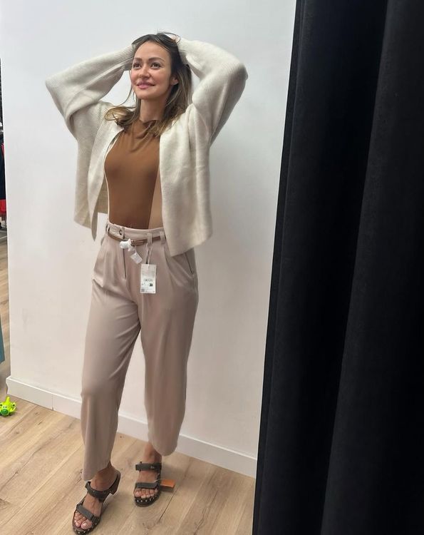 Mujer vestida de color beige, con cárdigan blanco y las manos detrás de la cabeza, en una tienda.