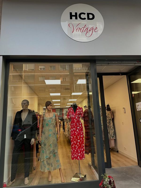 Fachada de tienda vintage HCD con escaparate de maniquíes con vestidos y un cartel.