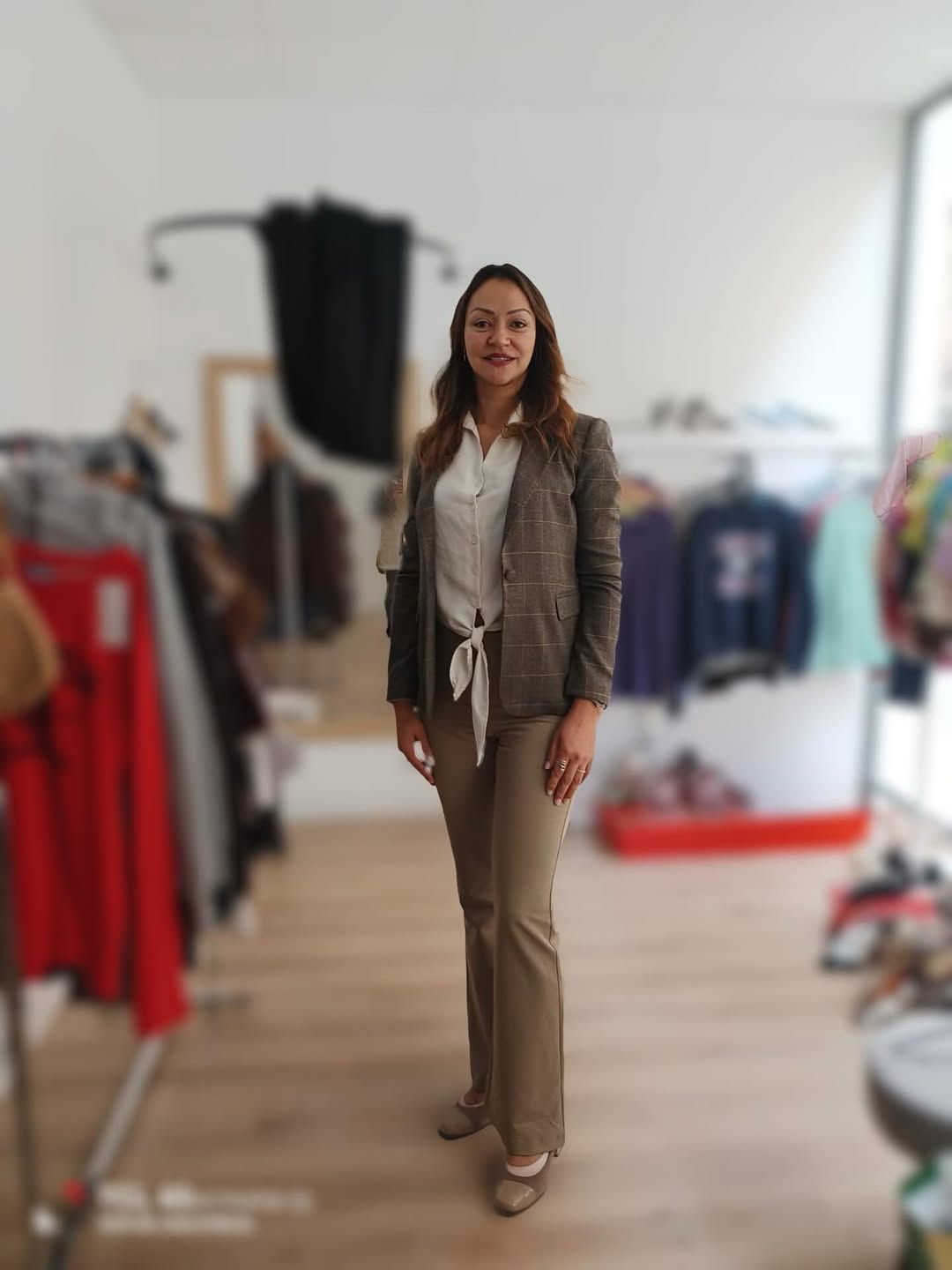 Mujer con blazer y pantalones posa dentro de una tienda de ropa, rodeada de estantes con prendas.