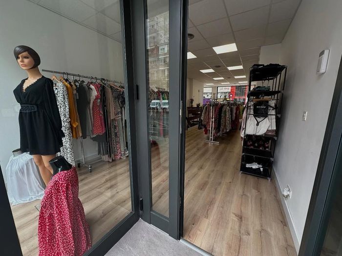 Interior de tienda de ropa con percheros, maniquí con vestido negro, suelo de madera y puerta abierta.