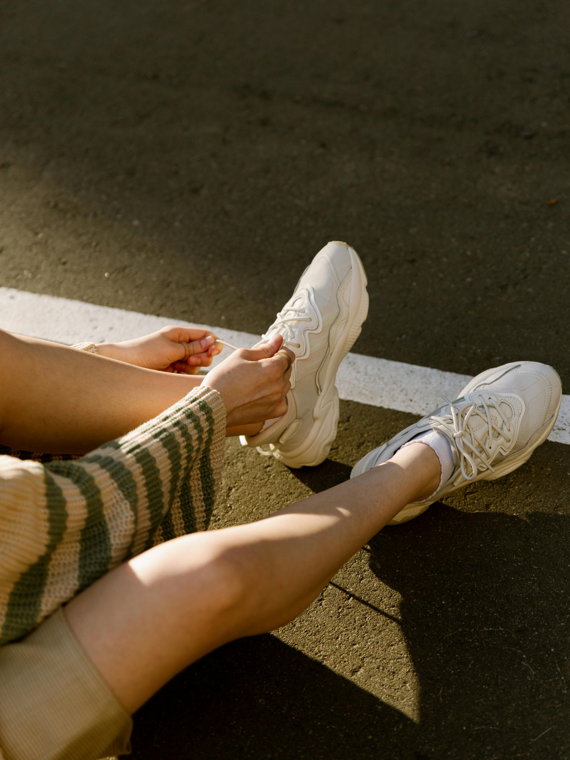 Persona sentada, atándose los cordones de unas zapatillas blanca