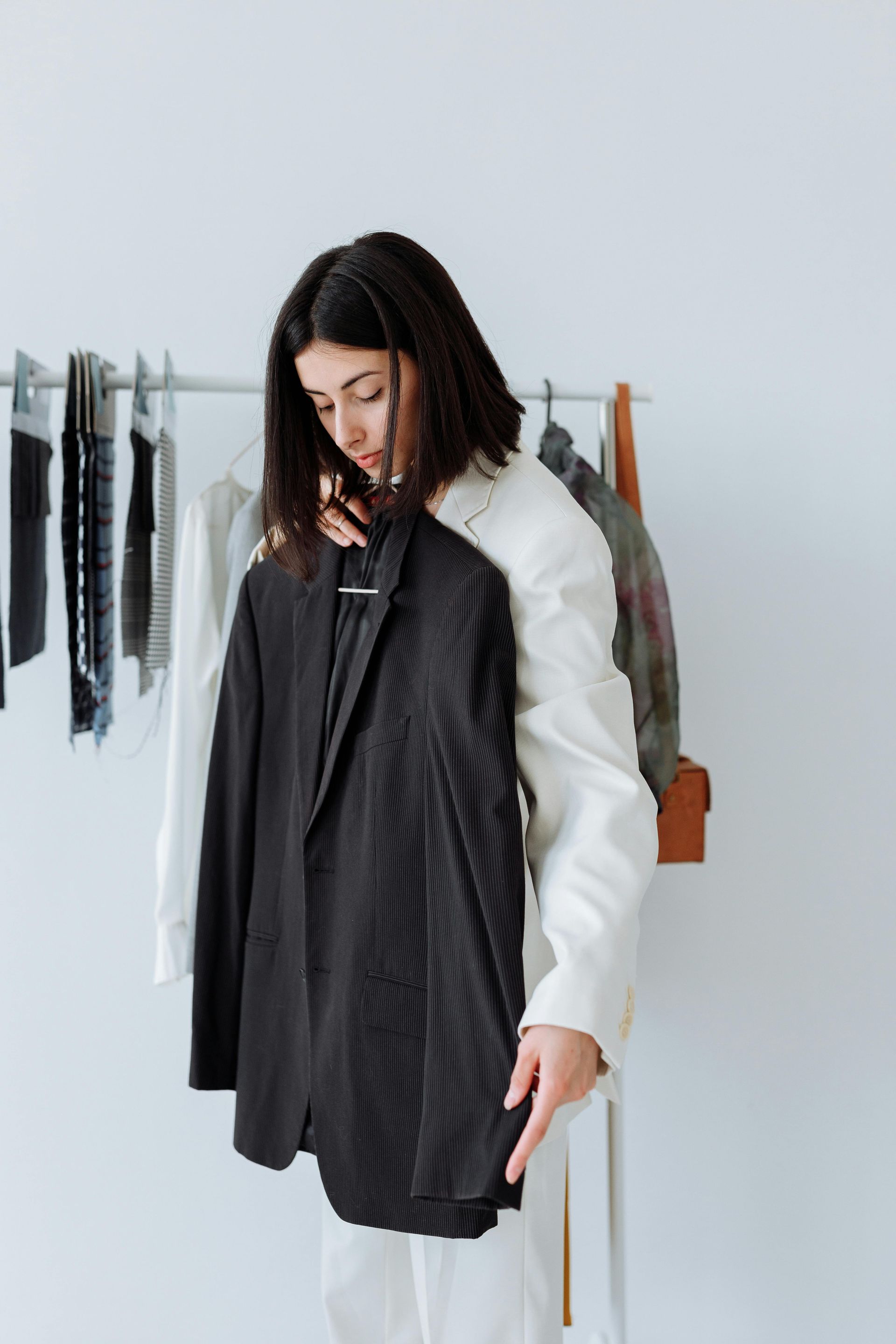 Mujer vestida de blanco sosteniendo un blazer negro frente a un perchero.