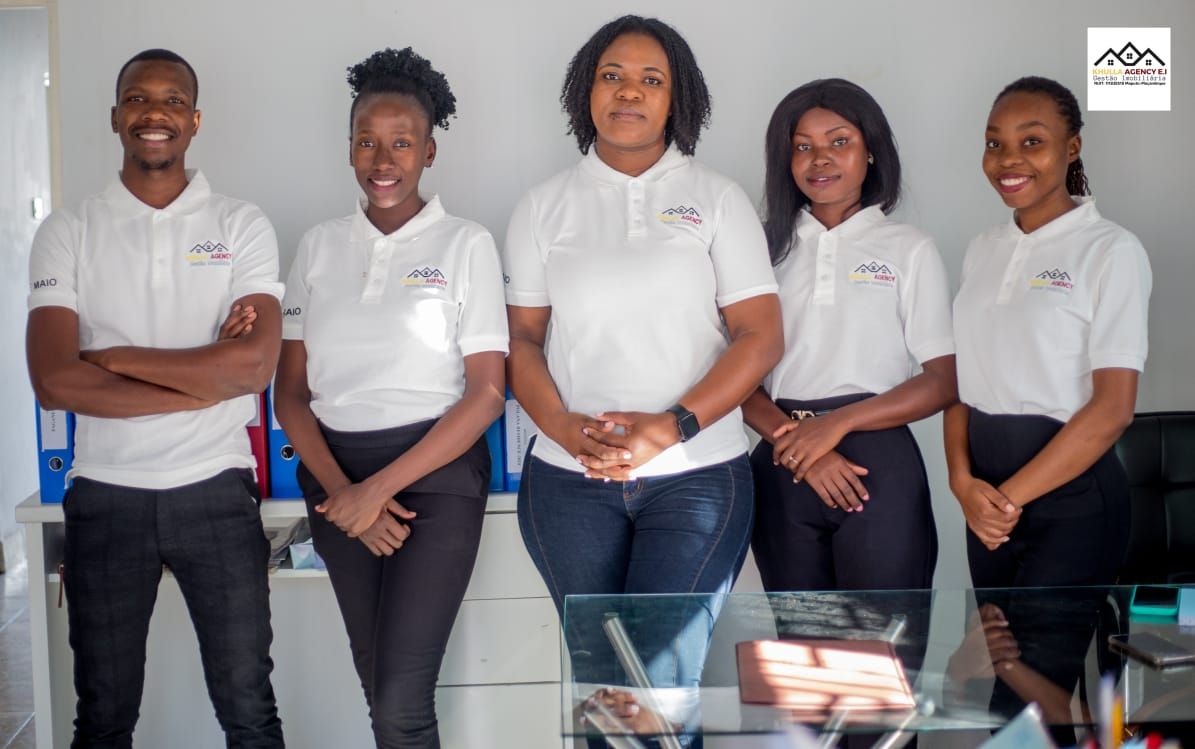 Five people, smiling, in matching white shirts and dark pants, pose in an office.