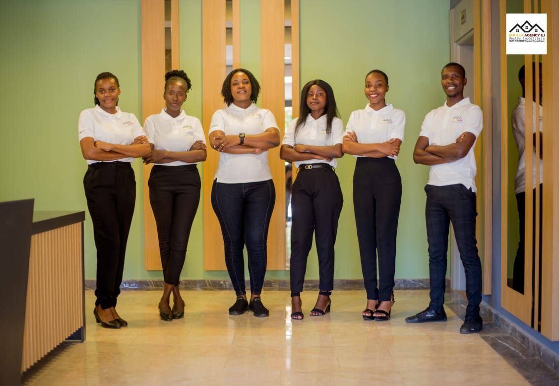 Six people in white shirts and black pants standing with crossed arms in a building.