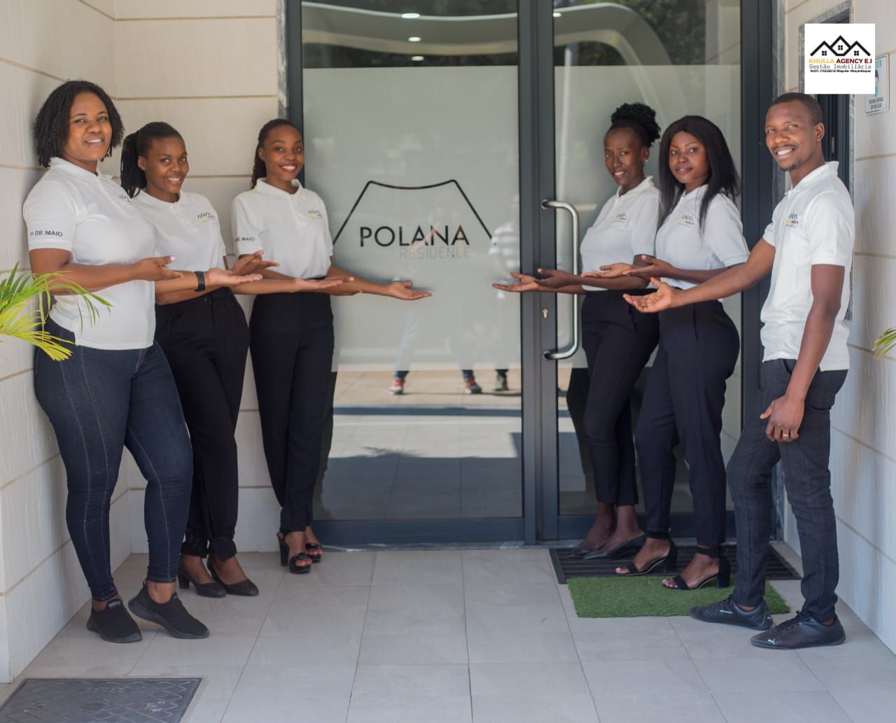 Group of people welcoming at a Polana business entrance. They wear matching white shirts and dark pants.