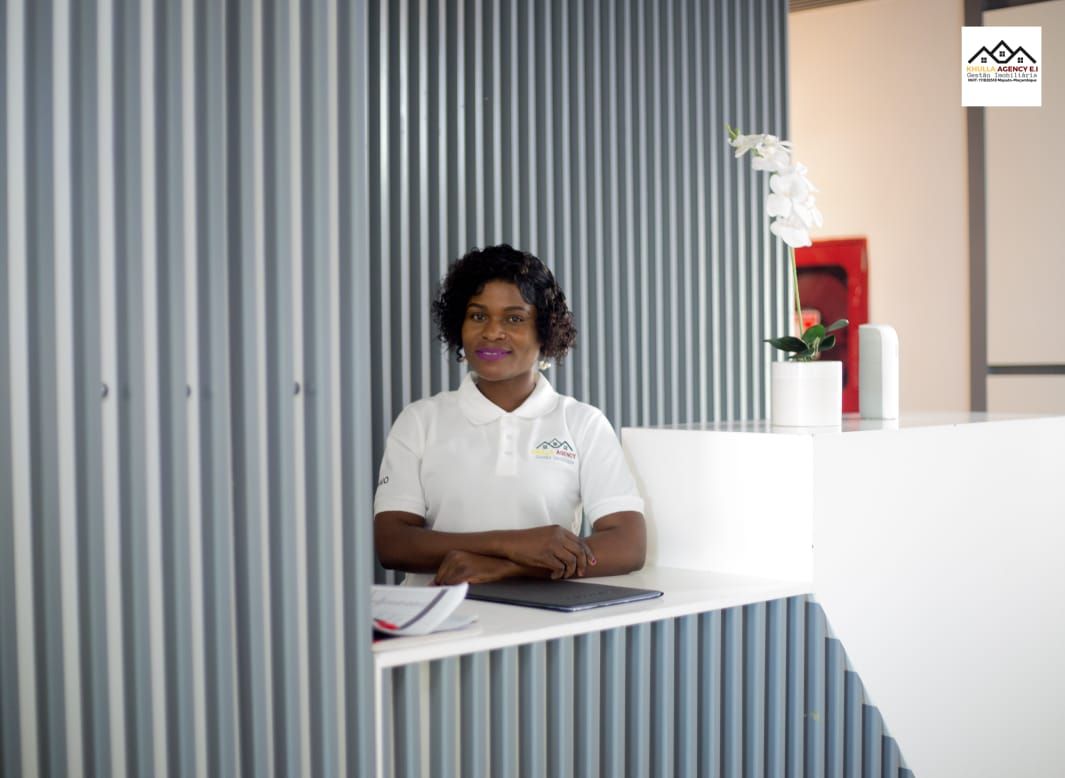 Woman in white shirt at a reception desk, arms crossed, in a modern office setting.