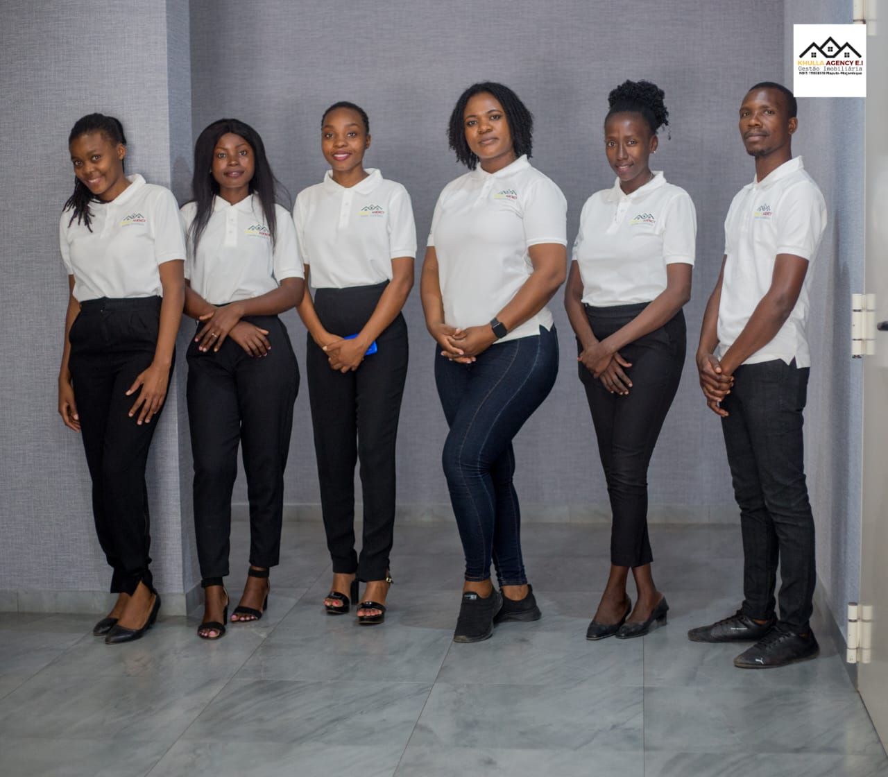 Six people in white polo shirts and dark pants, posing inside.